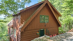 Une cabane en bois avec un toit à forte pente, une porte verte et un petit porche agrémenté de coussins rouges.