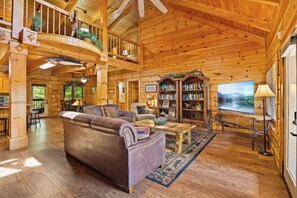 A spacious wooden interior with a large couch, a bookshelf, and a television.