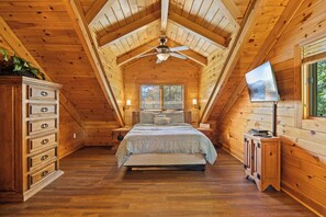 A bedroom with a sloped ceiling, a bed with a checkered bedspread, a dresser with multiple drawers, a nightstand, a lamp, and a television on a stand.