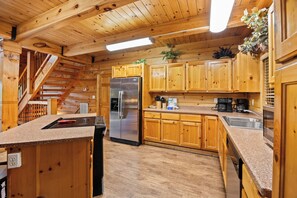 A wooden cabin interior with a kitchen, wooden cabinets, a stainless steel refrigerator, a coffee maker, and a staircase.