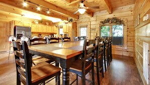 A wooden cabin-style kitchen with a large dining table, chairs, and a ceiling fan.