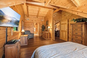A wooden cabin interior with a bed, a desk, a chair, a dresser, and a painting of a mountain landscape.