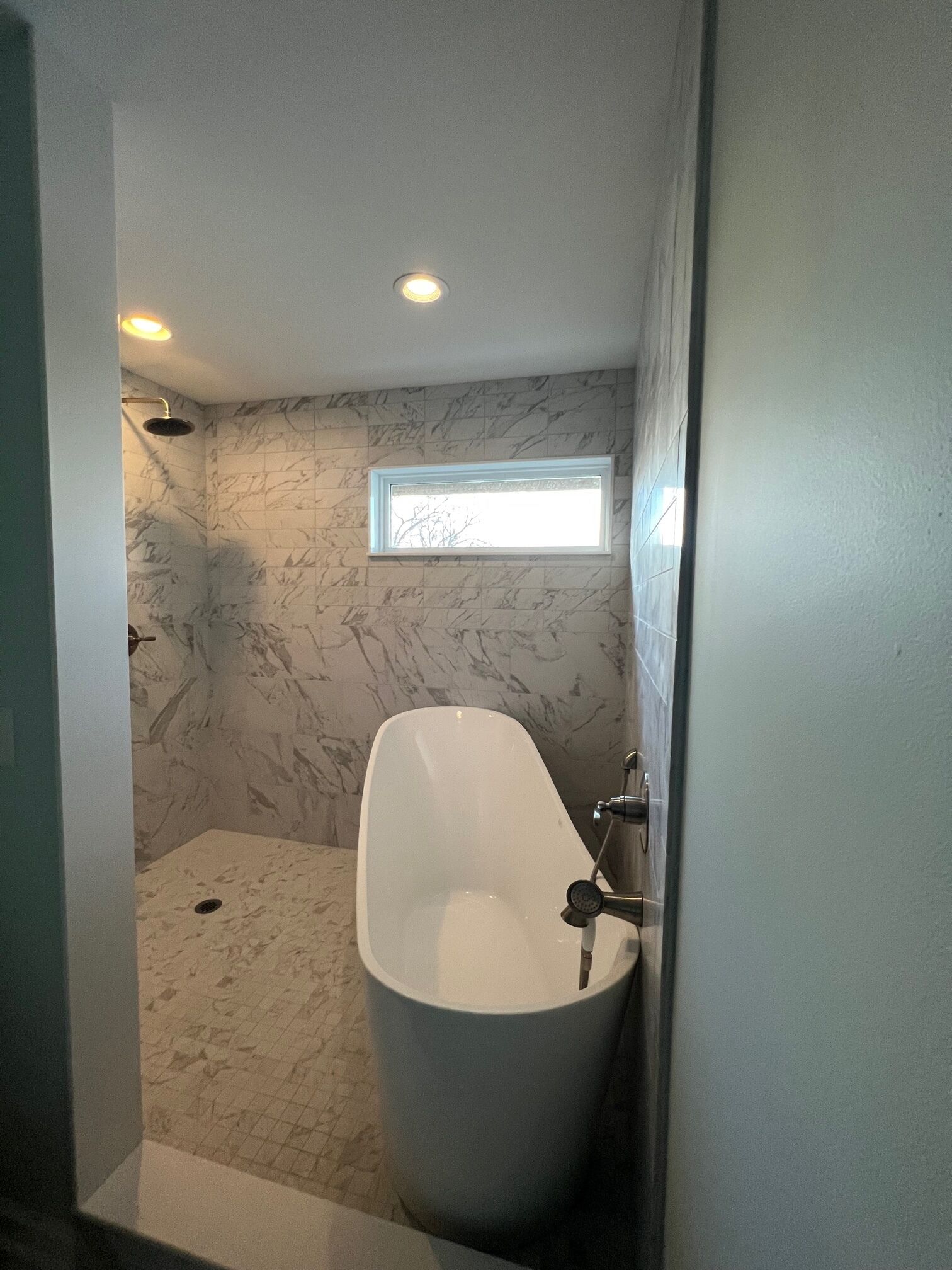 Une salle de bain moderne avec une baignoire sur pieds, des murs en marbre et un puits de lumière.