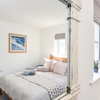 Quarto com cama, almofadas, manta, pintura e janela.