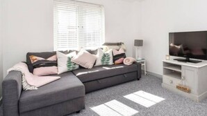 A modern living room with a grey sectional sofa, a flat-screen TV, and a lamp on a side table. - The Little House, Boutique Home Near the sea (Chichester)