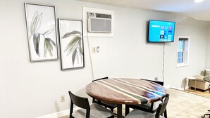 Ein Essbereich mit einem runden Tisch, vier Stühlen, einem an der Wand befestigten Flachbildfernseher und zwei gerahmten Pflanzenbildern.