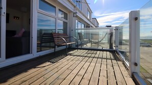 A wooden deck with a glass balustrade, a bench, and a view of the sea. - No. 28 Contemporary Beach Side Property With sea Views (Chichester)