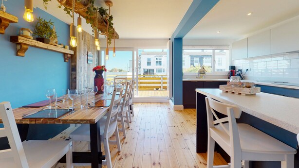 A modern kitchen with wooden countertops, white cabinets, and a dining area with a wooden table and chairs. - No. 28 Contemporary Beach Side Property With sea Views (Chichester)