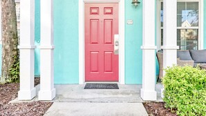 Una casa color turchese con una porta rossa, colonne bianche e un piccolo portico.