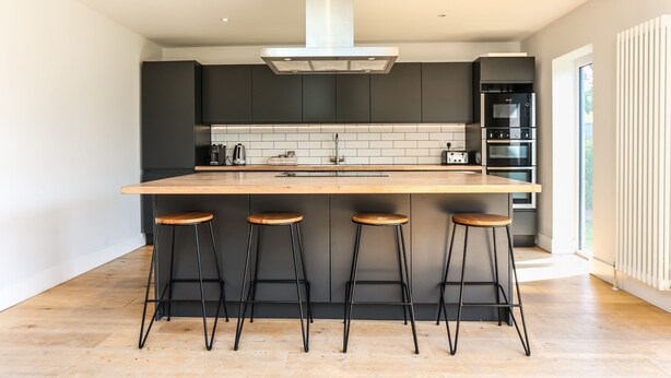 Cozinha moderna com ilha central, banquetas pretas e eletrodomésticos embutidos.