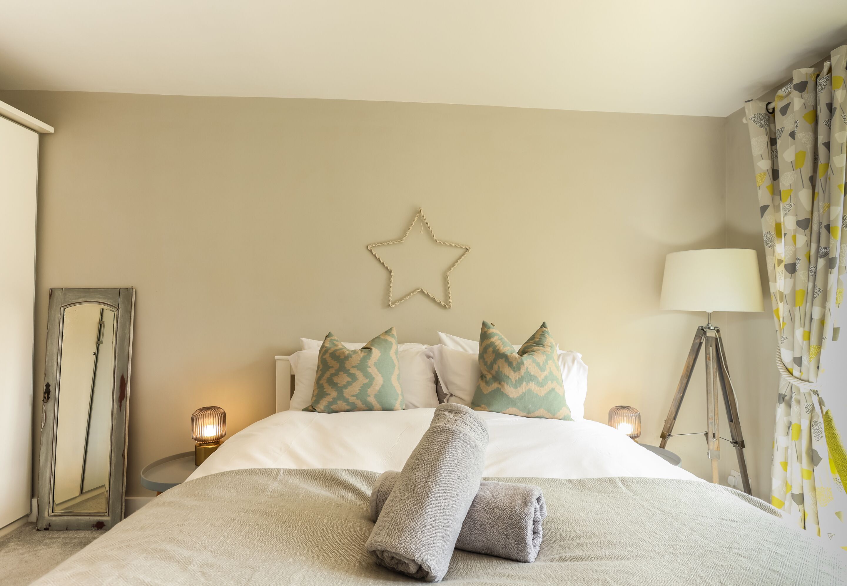 Ein ordentlich bezogenes Bett mit einer Sternen-Dekoration an der Wand, einer Lampe und einer Stehlampe am Rand.