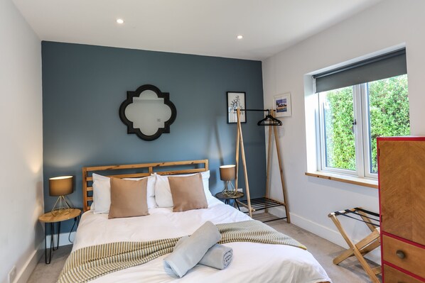 Een netjes opgemaakte slaapkamer met een bed, nachtkastjes, een hanglamp en een raam met uitzicht op groen.