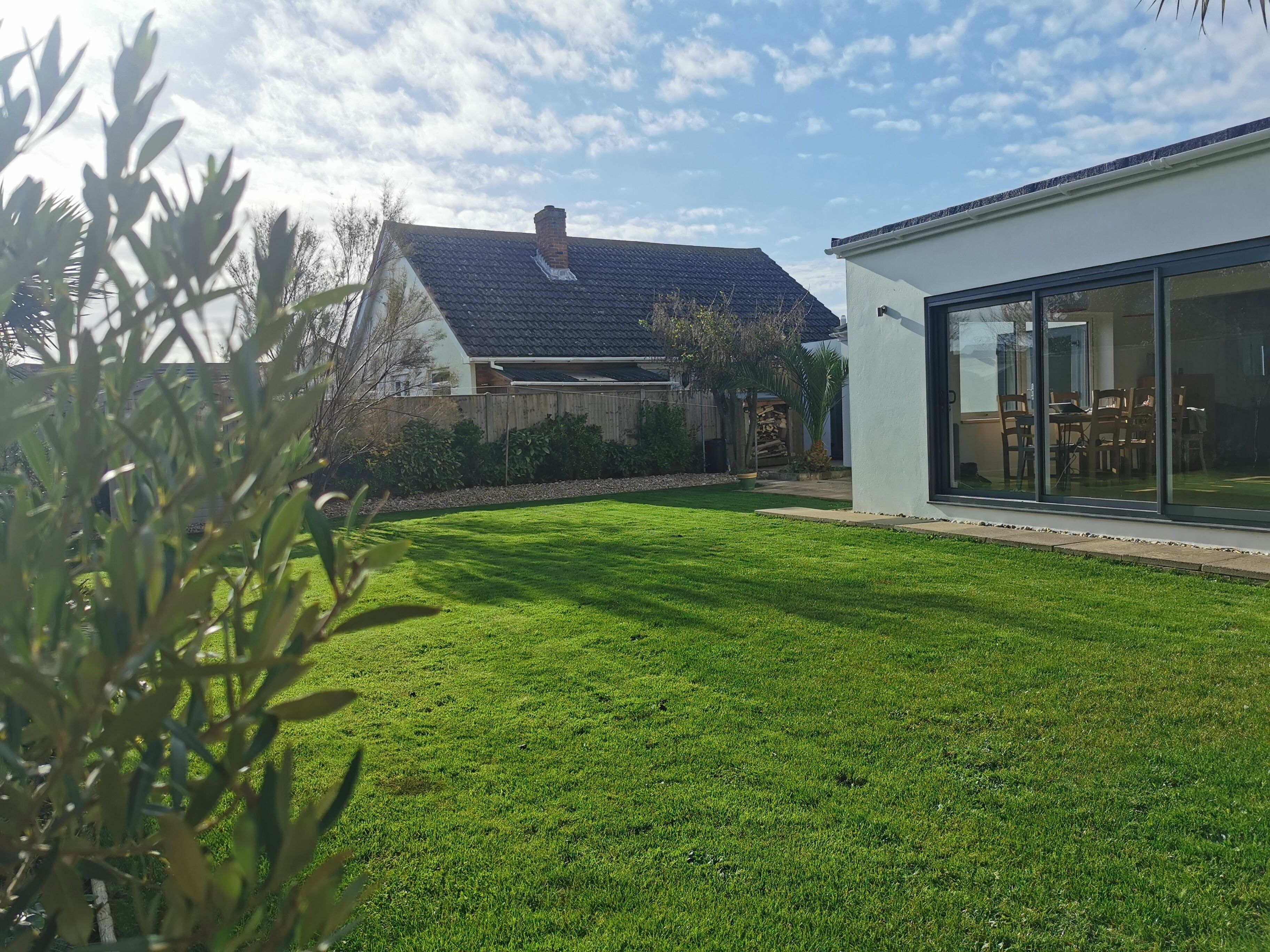 A modern house with a well-maintained lawn, a wooden fence, and a large glass door leading to an outdoor dining area.