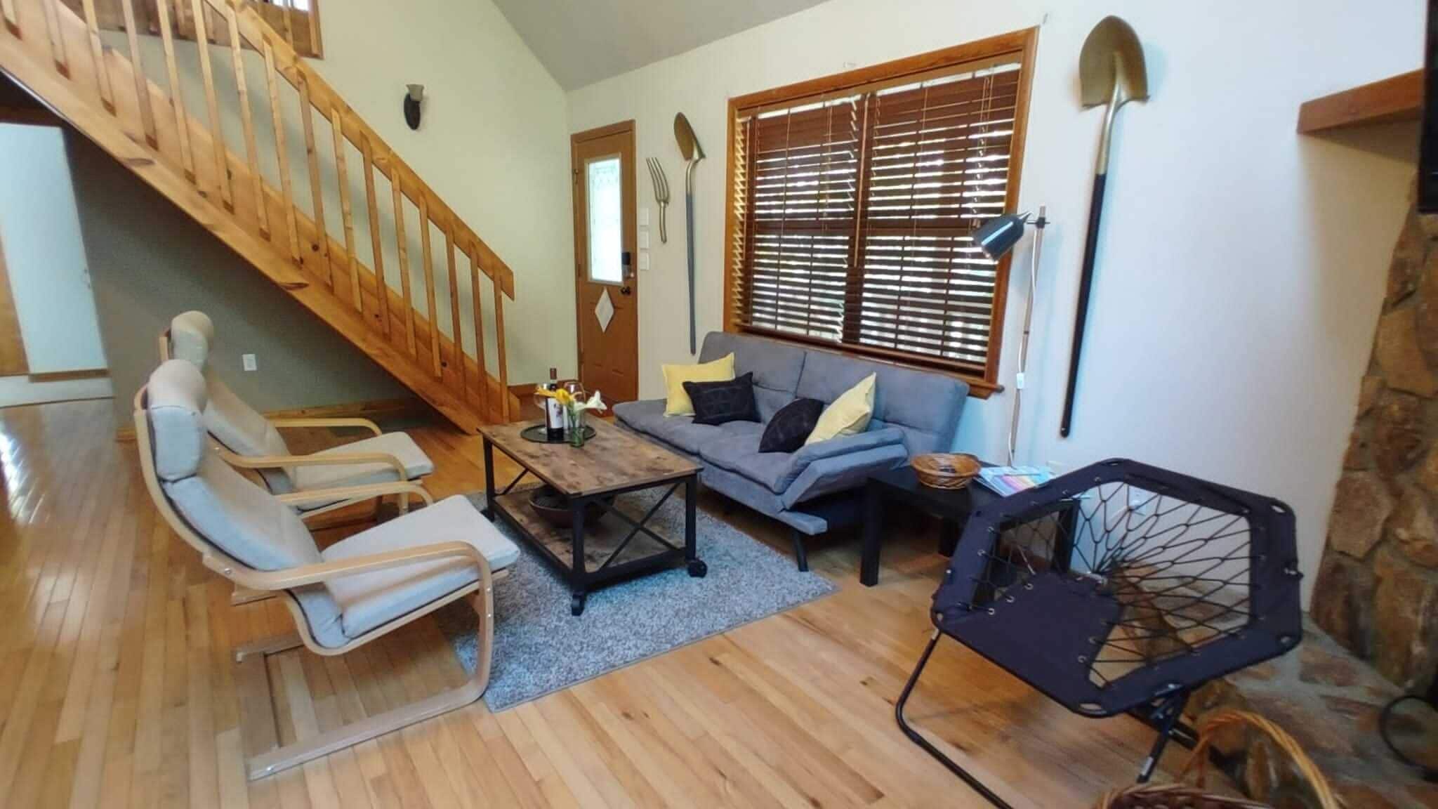 A living room with a wooden staircase, a sofa, a coffee table, and a grill.