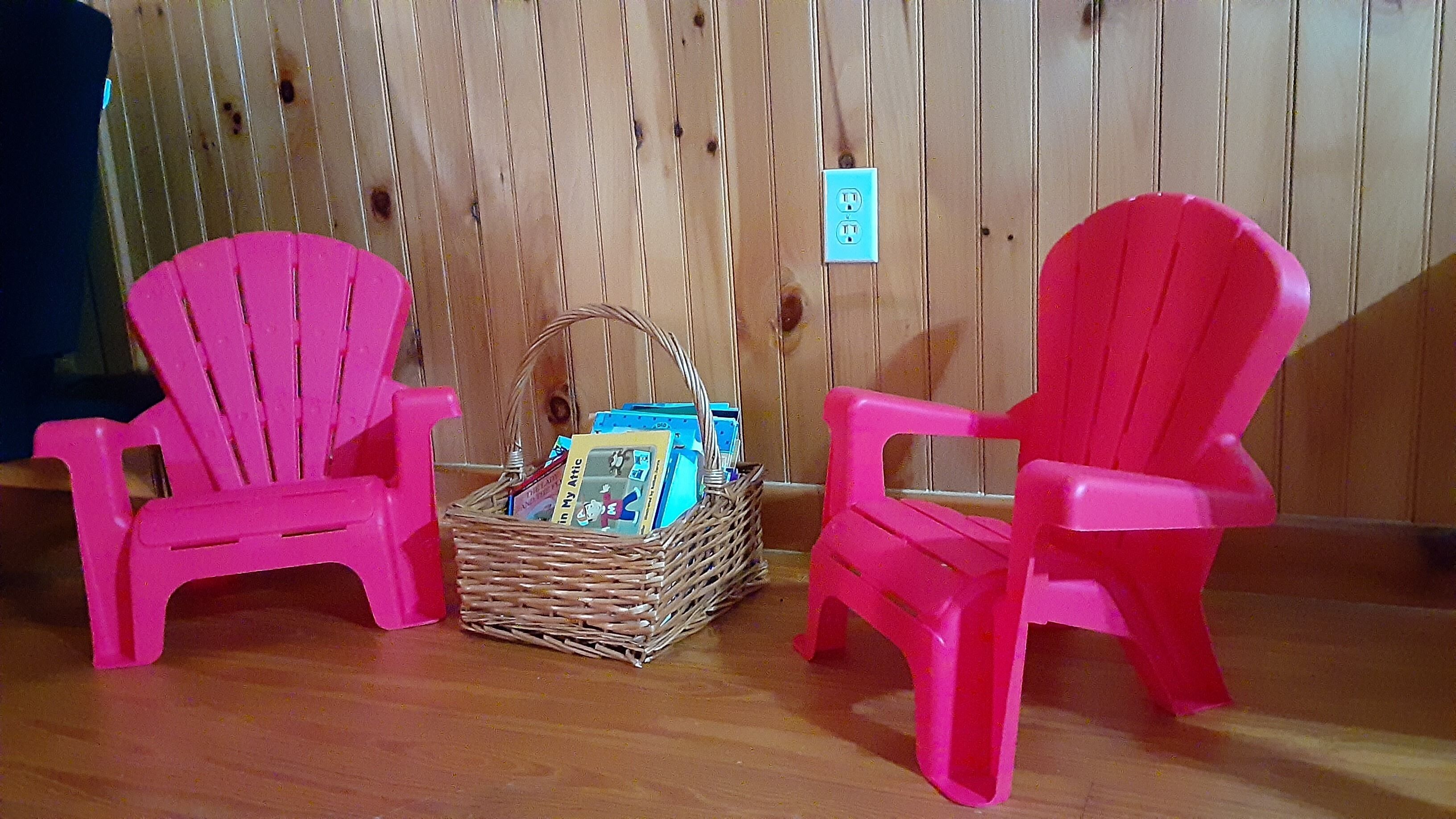 Deux chaises roses et un panier en osier contenant des magazines, le tout posé sur un plancher en bois.
