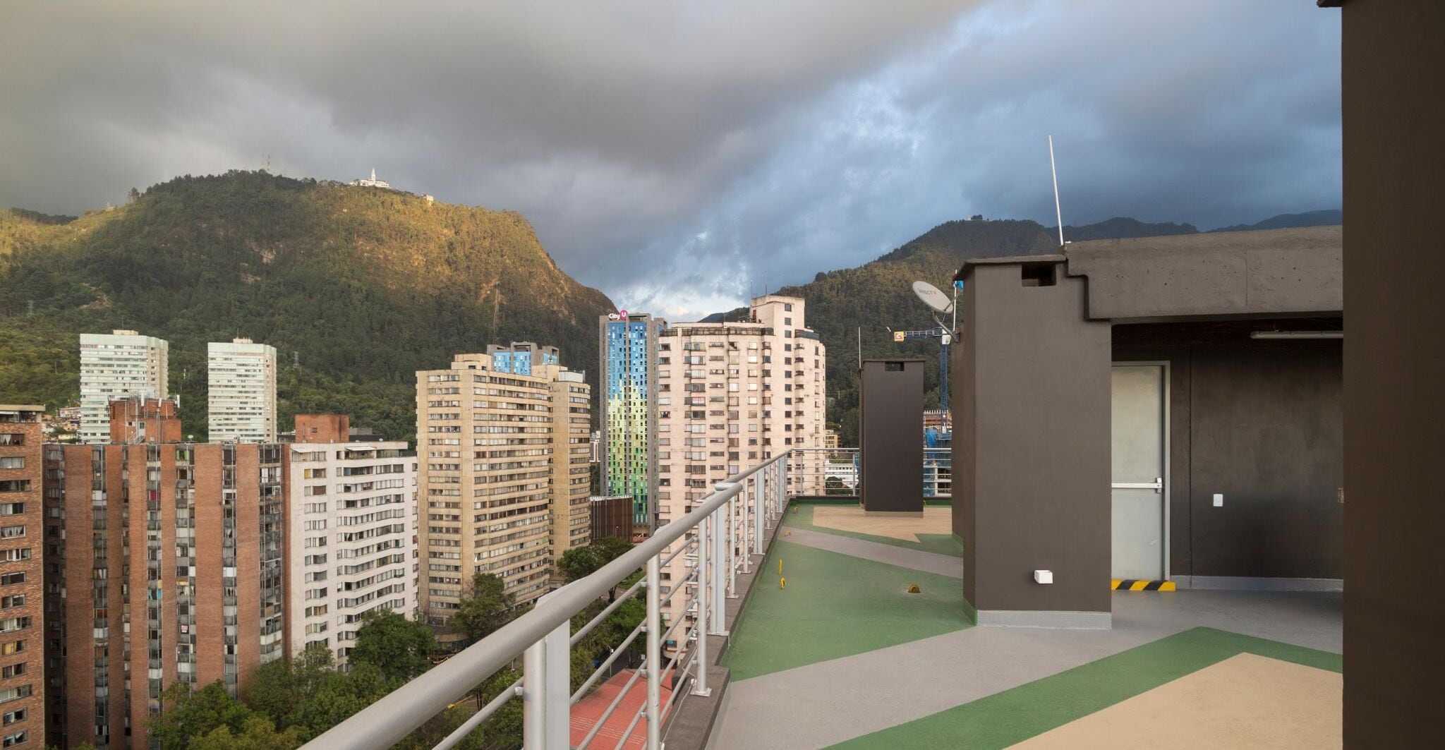 A residential area with high-rise buildings, a sports field, and a mountainous backdrop.