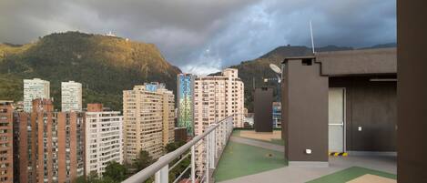 A residential area with high-rise buildings, a sports field, and a mountainous backdrop.
