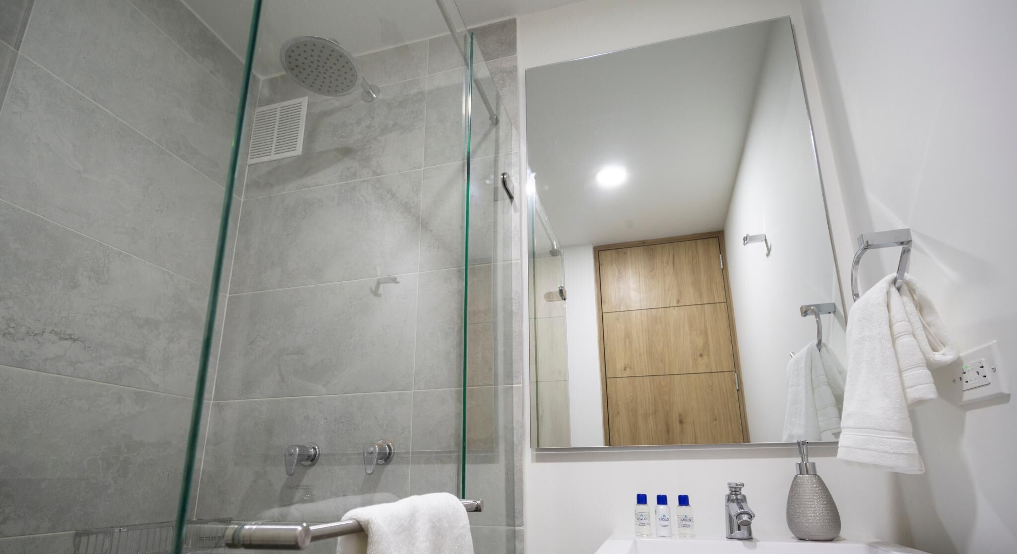 Ein modernes Badezimmer mit Duschkabine aus Glas, einem Holzkabinet, einem weißen Waschbecken und einem Spiegel.