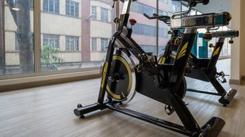 A stationary bike in a room with large windows, a wooden floor, and a view of a building outside.