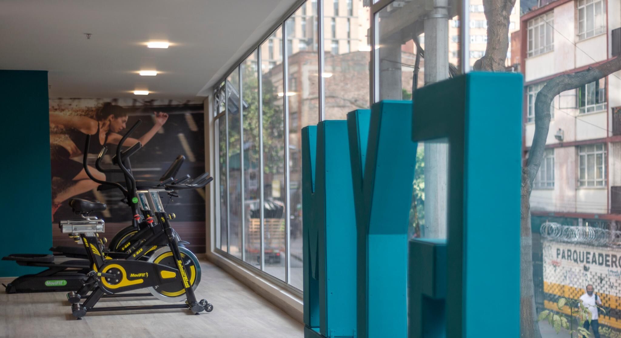 A gym with stationary bikes, teal exercise equipment, and a mural of a person cycling.