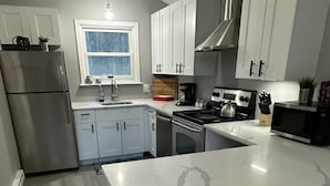 A modern kitchen with a marble countertop, stainless steel appliances, and white cabinetry.