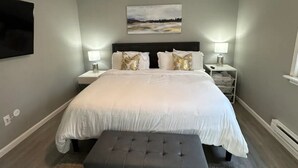 A bedroom with a bed, bedside tables, a ceiling fan, a bench, and a painting on the wall.
