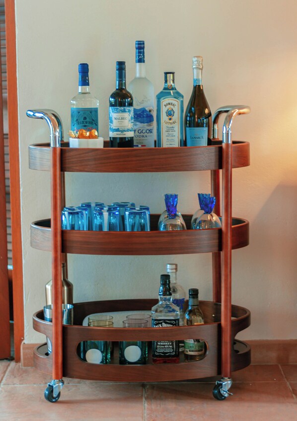 A wooden three-tiered cart with various bottles and glasses. - Villa Rosso Di Sera: 2 Minute Walk from the Beach (Chalk Sound)