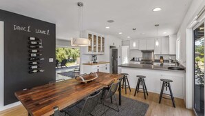 Una cocina moderna con una mesa de comedor de madera, taburetes de bar y una estantería para vinos en la pared.