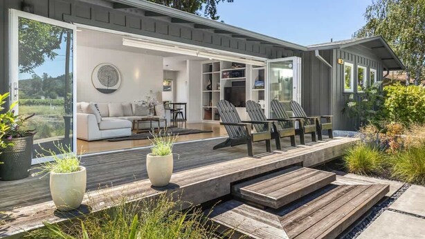 Una casa moderna con terraza, mobiliario exterior y un amplio ventanal que da a un espacio interior.