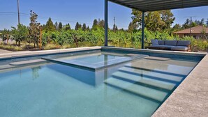 Una piscina con piso de vidrio, rodeada por un porche cubierto y vistas a un viñedo.