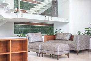 Ein modernes Wohnzimmer mit einer Sofagarnitur, einem Holztisch und einem großen Fenster mit Blick auf Grünflächen.