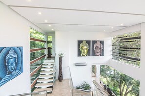 A modern interior with a glass staircase, artwork, and a view of greenery. - Luxury Villa #10 Private Pool, Oceanview, & Complimentary Concierge Services (Playa Hermosa)