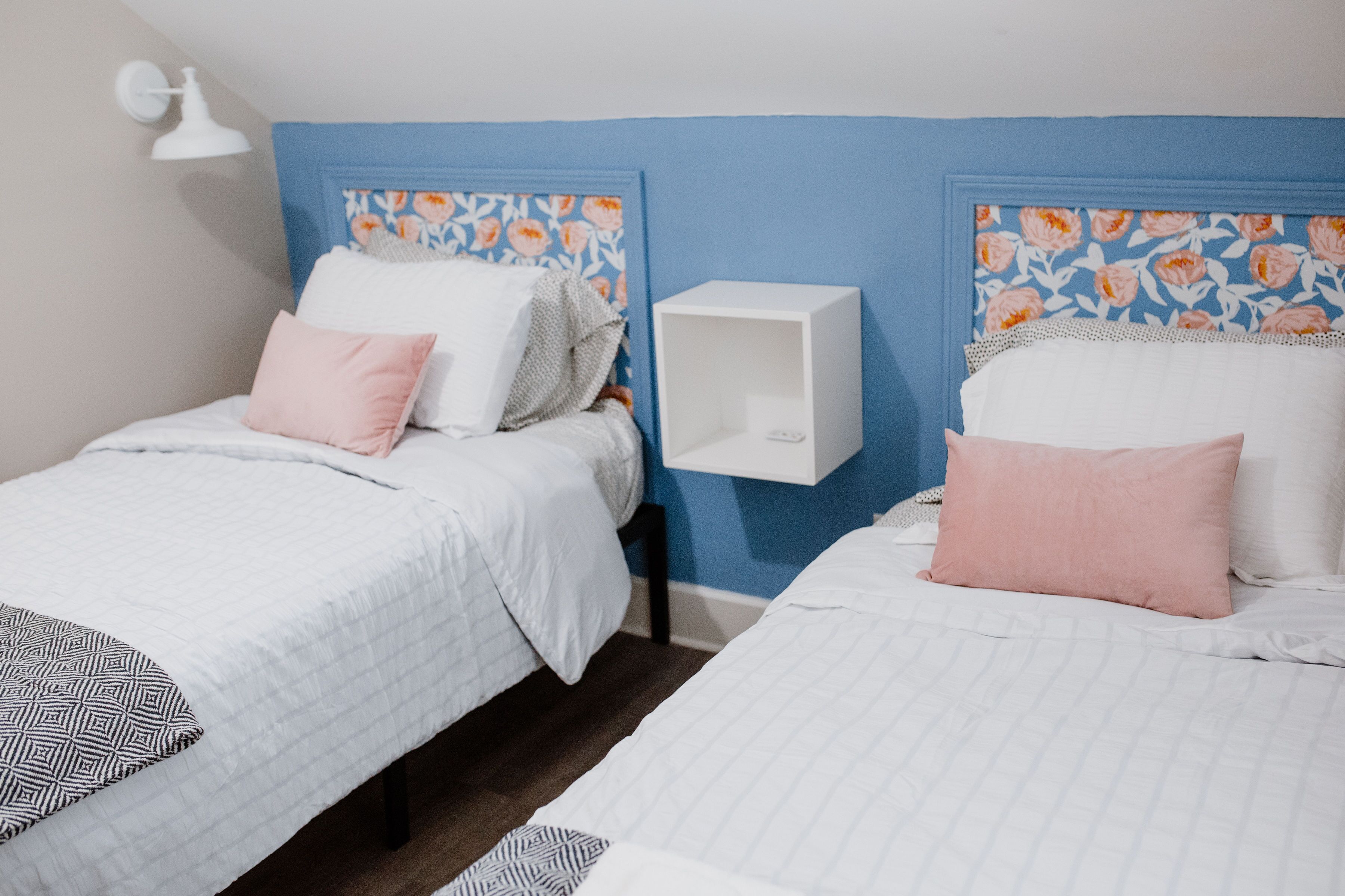 Two single beds with floral headboards, a white bedside table, and a wall-mounted light fixture.