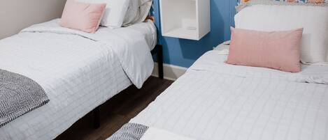 Two single beds with floral headboards, a white bedside table, and a wall-mounted light fixture.
