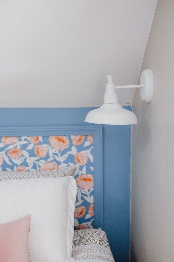 A bedroom with a blue accent wall, a white bed with a pink pillow, and a white wall-mounted lamp. - Family Friendly | Clean | Quiet (Louisville)