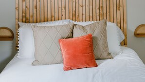 Ein Bett mit weißer Bettwäsche, einem Holterslattenkopf und mehreren Kissen, darunter eines rotes.