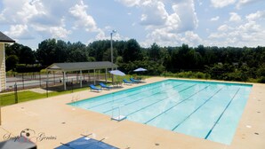 Ein rechteckiger Pool mit klarem, blauem Wasser, umgeben von einer gefliesten Liegefläche. Liegestühle und Sonnenschirme befinden sich unter einem überdachten Bereich.