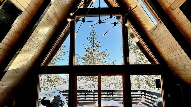 A cozy room with a high ceiling and wooden beams, large windows offering a view of a snowy outdoor area. - Modern A-Frame Cabin in Mammoth (Mammoth Lakes)