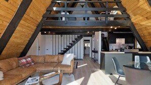 A loft-style interior with a wooden ceiling, a sofa, a glass coffee table, and a kitchen area. - Modern A-Frame Cabin in Mammoth (Mammoth Lakes)