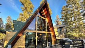A modern cabin with a sloped roof, large glass windows, and a deck with outdoor seating. - Modern A-Frame Cabin in Mammoth (Mammoth Lakes)