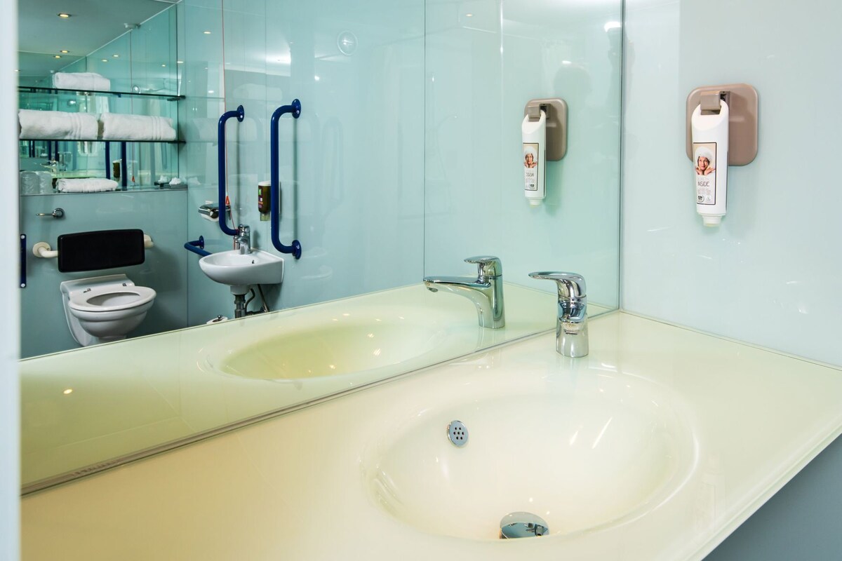 A modern bathroom with a large mirror, a white sink, a handheld showerhead, and a toilet.