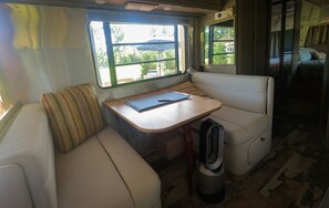Interior acogedor de una caravana, con una zona de estar con cojines, una mesita y una ventana que ofrece vistas al exterior.