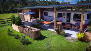 A recreational vehicle (RV) parked under a wooden pavilion with a hammock and outdoor furniture.