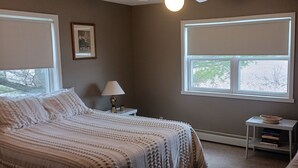 Un dormitorio con cama, mesita de noche, lámpara y ventana con vista a árboles.