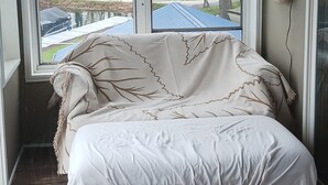 Una habitación con cama, una mesa y ventana con vistas a una casa y árboles.