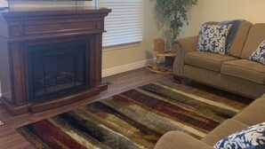 Ein Wohnzimmer mit Kamin, einer Couch, einem Streifenmuster-Teppich, einem Fernseher und einem Deckenventilator.