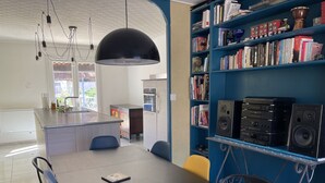 A modern kitchen with a central island, a dining area with a black table, and a bookshelf filled with books and audio equipment. - Charming property surrounded by vineyards near St Chinian (Pierrerue)