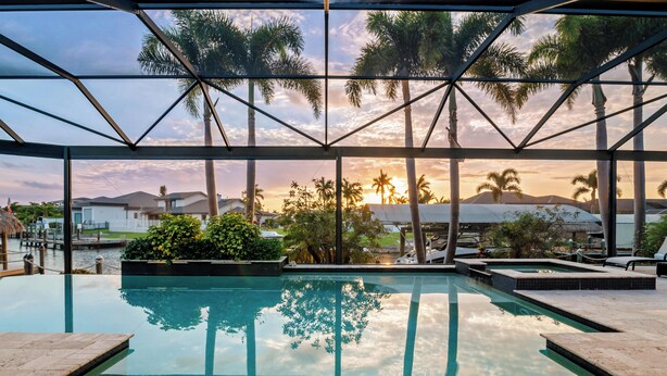 Una piscina con cerramiento de vidrio, rodeada de palmeras y vistas al atardecer.