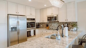Una cocina con armarios blancos, electrodomésticos de acero inoxidable, una encimera de granito y una araña.