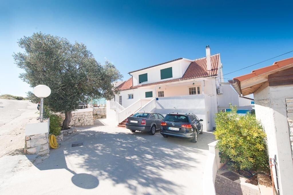 Une maison à deux étages, avec un toit recouvert de tuiles, un escalier menant à l’étage supérieur et deux voitures garées dans l’allée.